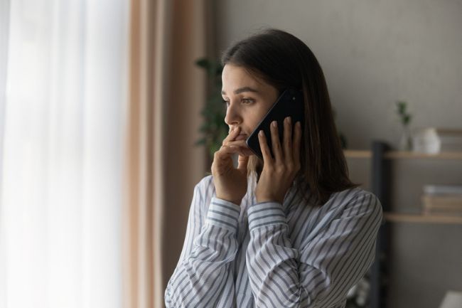 A woman, looking worried, calls someone on the phone